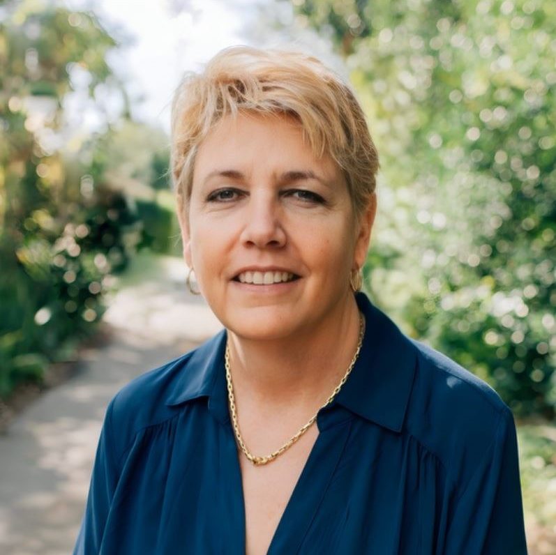 A woman named Kim West with short blonde hair wearing a blue shirt.