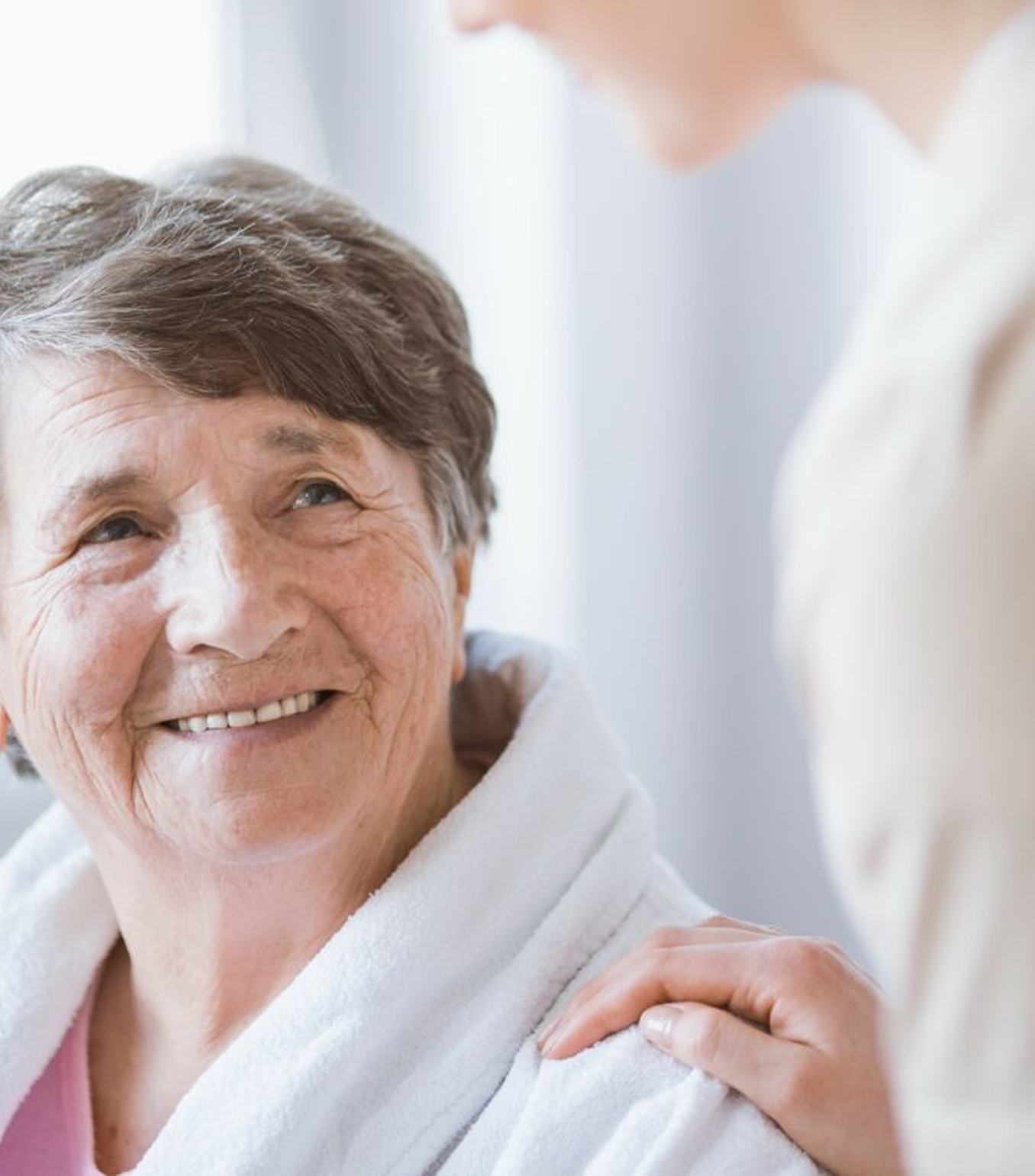 A smiling woman holds the hand of an elderly woman, showcasing warmth and support during a transportation appointment.