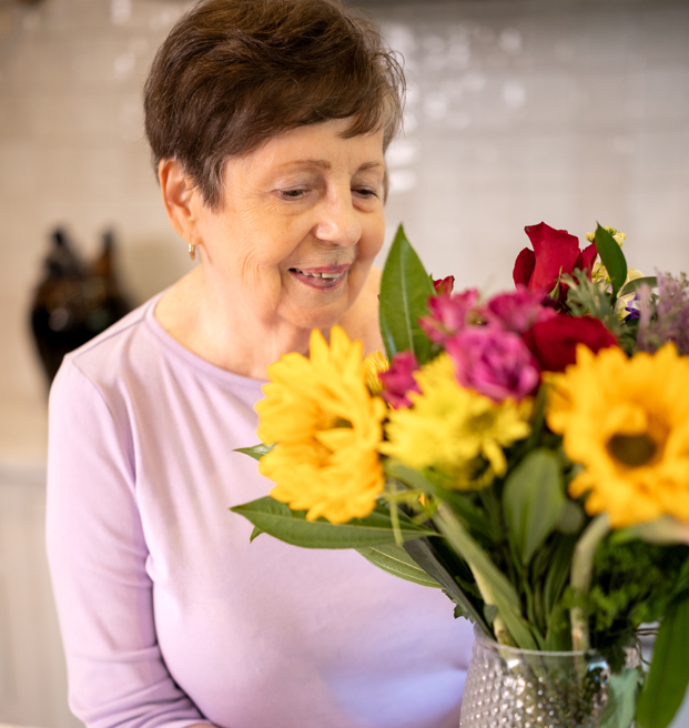 A woman gently holds a vase filled with colorful flowers, symbolizing care and compassion in end-of-life support.