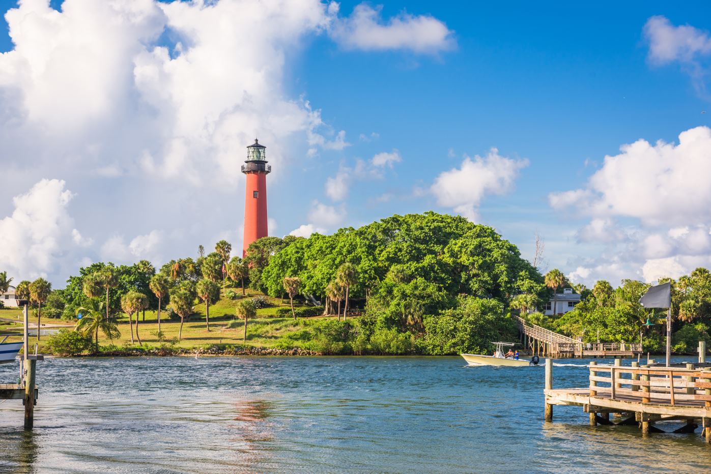 A lighthouse stands by the water, accompanied by a dock and trees, in a scenic view of Jupiter's coastline.
