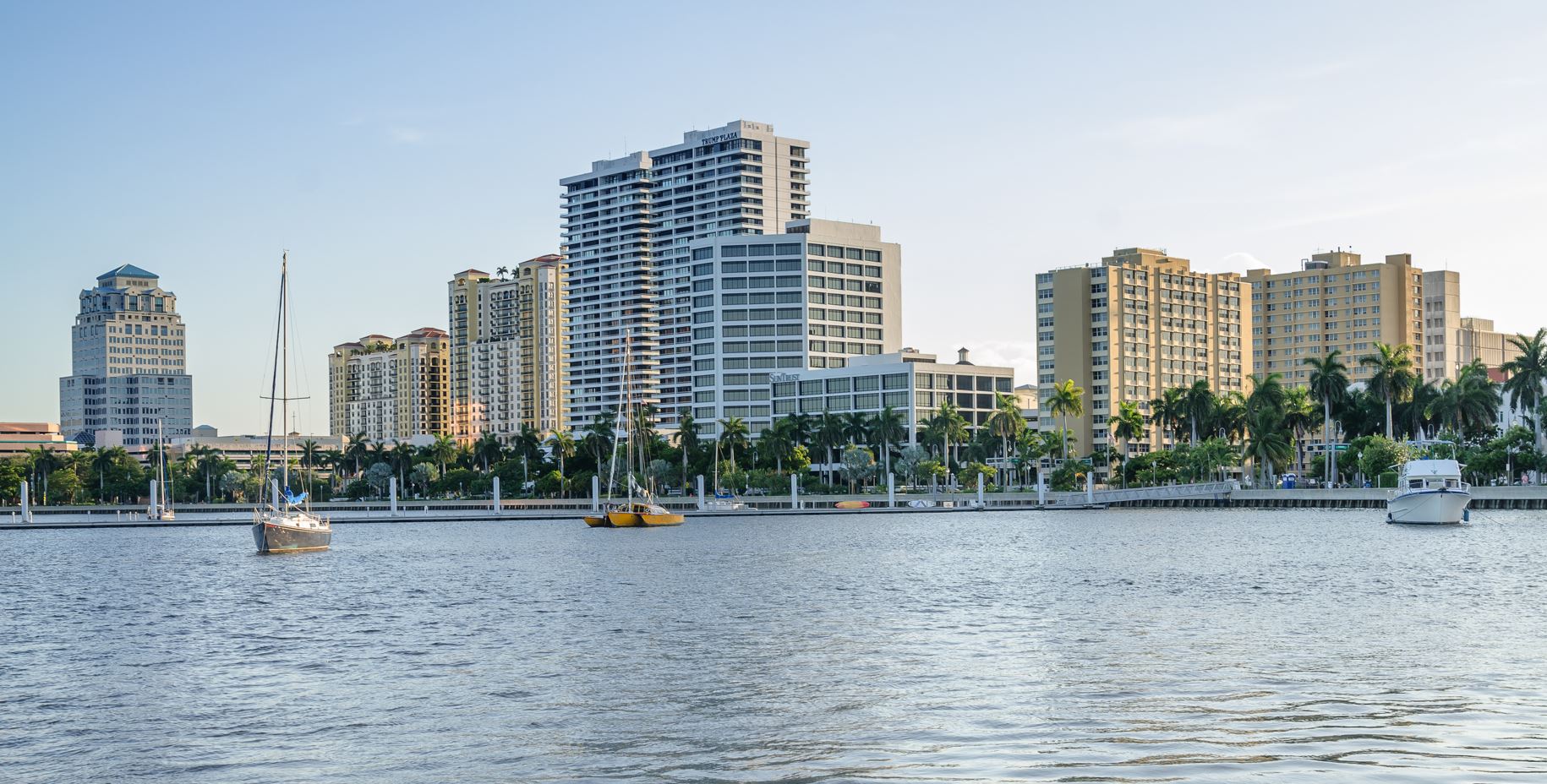 A serene body of water reflecting the sky, located in West Palm Beach, surrounded by lush greenery.