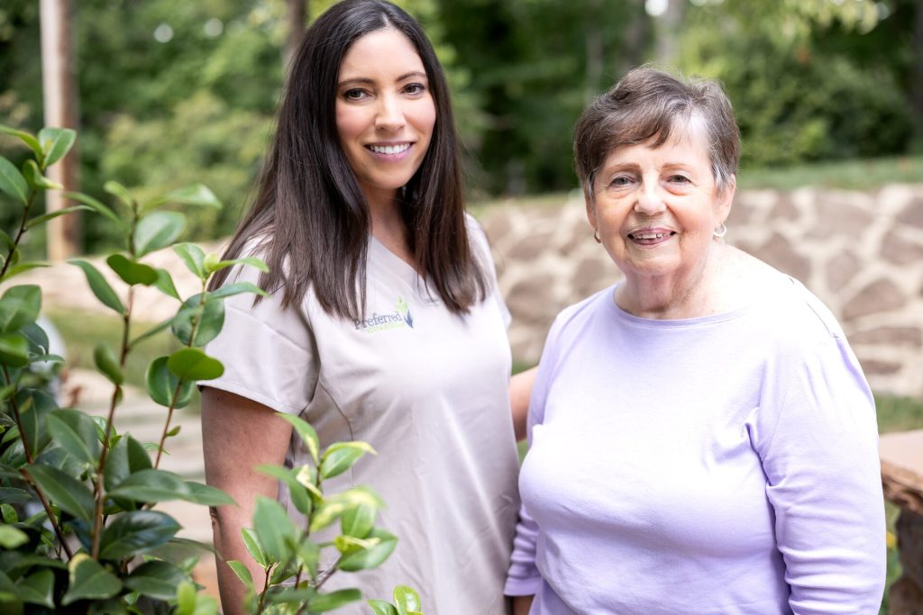 Caregiver and senior smiling together in a garden — companionship and connection in home care