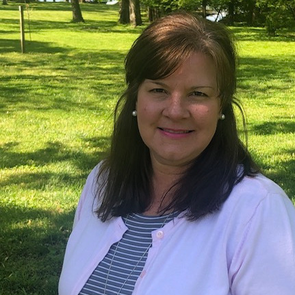 A woman in a pink cardigan stands in a park, representing Lisa Barry, Transition Liaison.