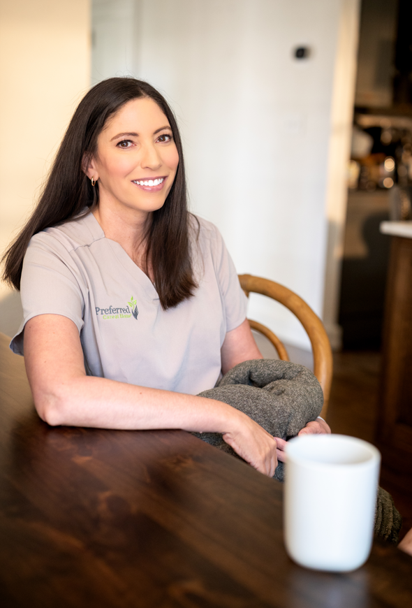 A woman in a gray shirt sits at a table, holding a cup of coffee, appearing thoughtful and relaxed.