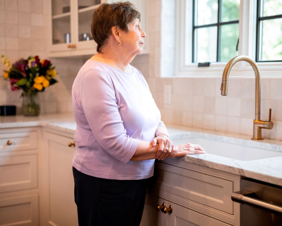 In a kitchen, a woman looks out the window, capturing a peaceful moment within a dementia care environment.