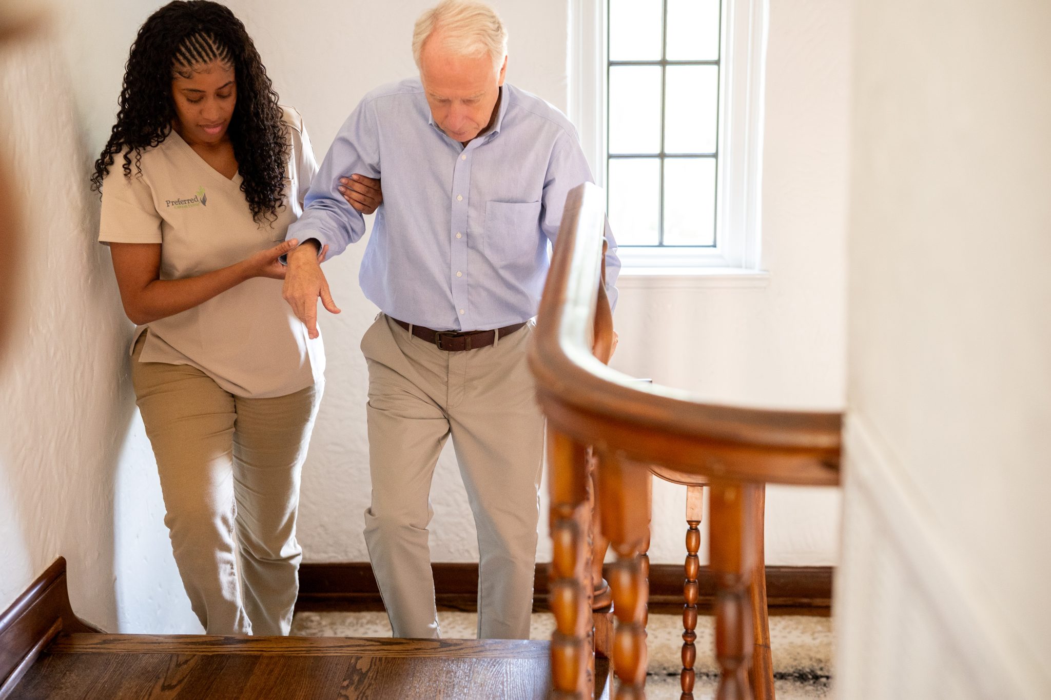 A woman assists an older man as he climbs stairs, demonstrating personal care and support.