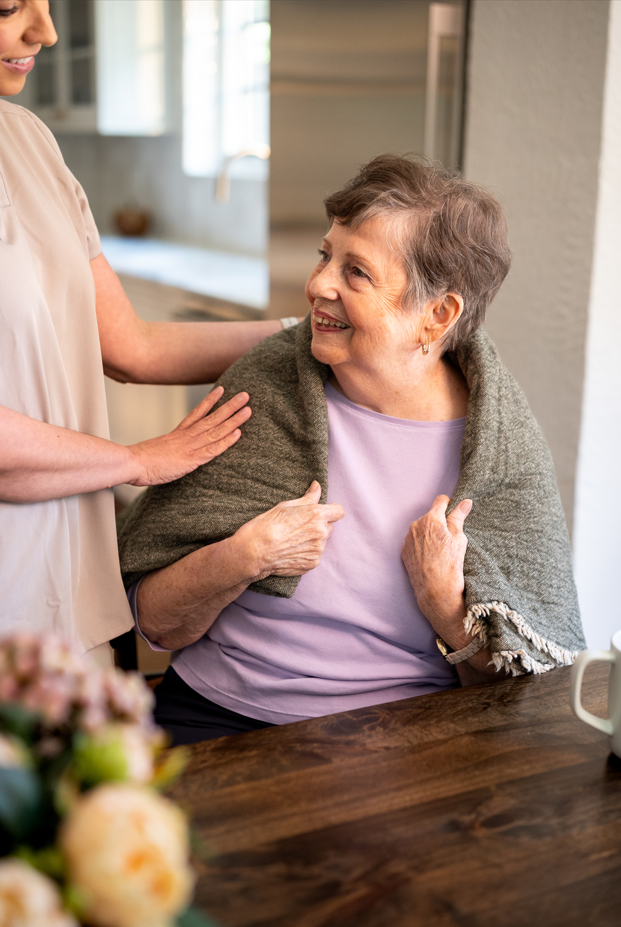 A woman assists an older woman in adjusting her scarf, showcasing a moment of care and companionship.