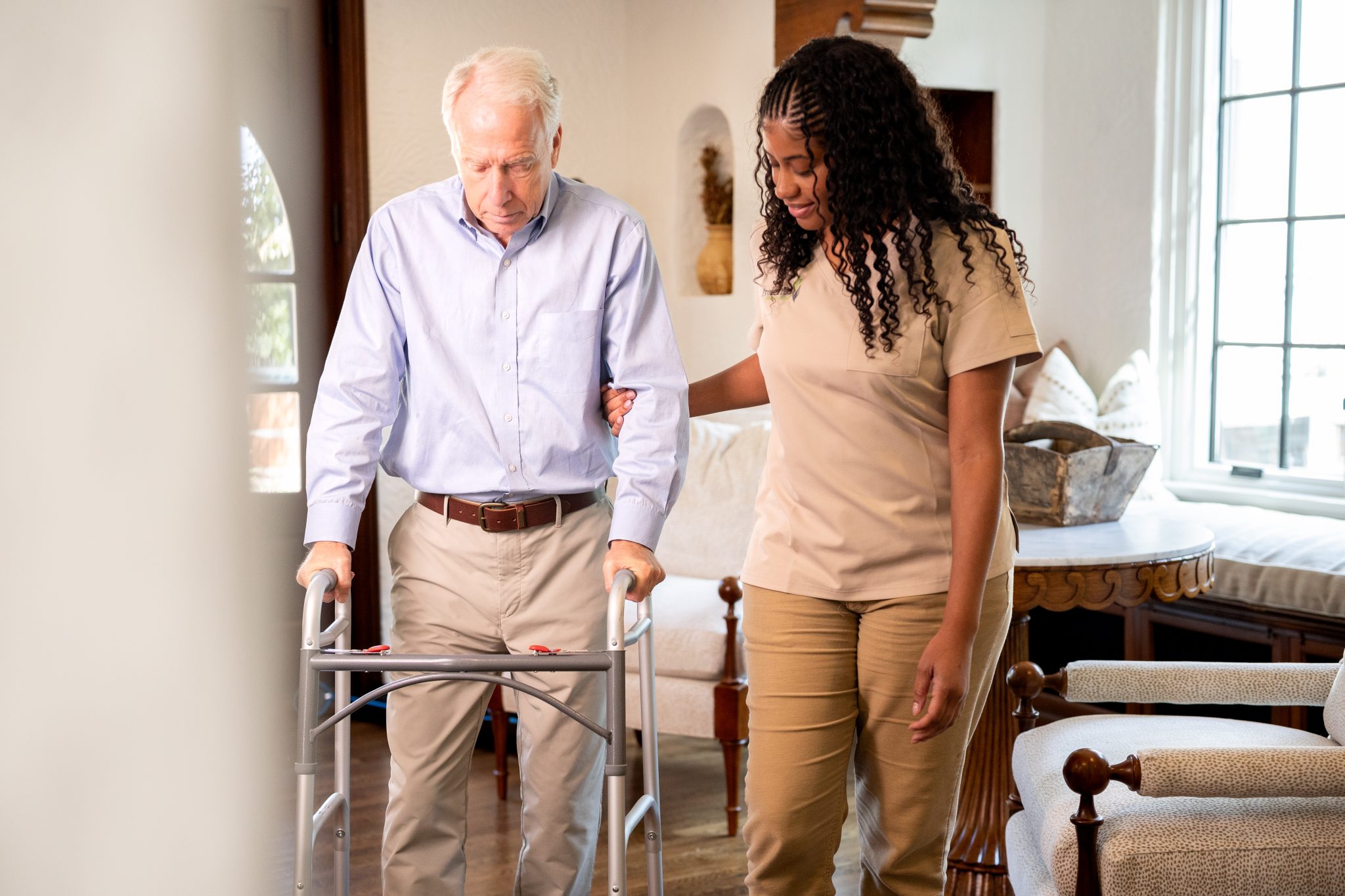 A woman assists an elderly man with a walker, providing support for safe mobility and personal care during recovery.