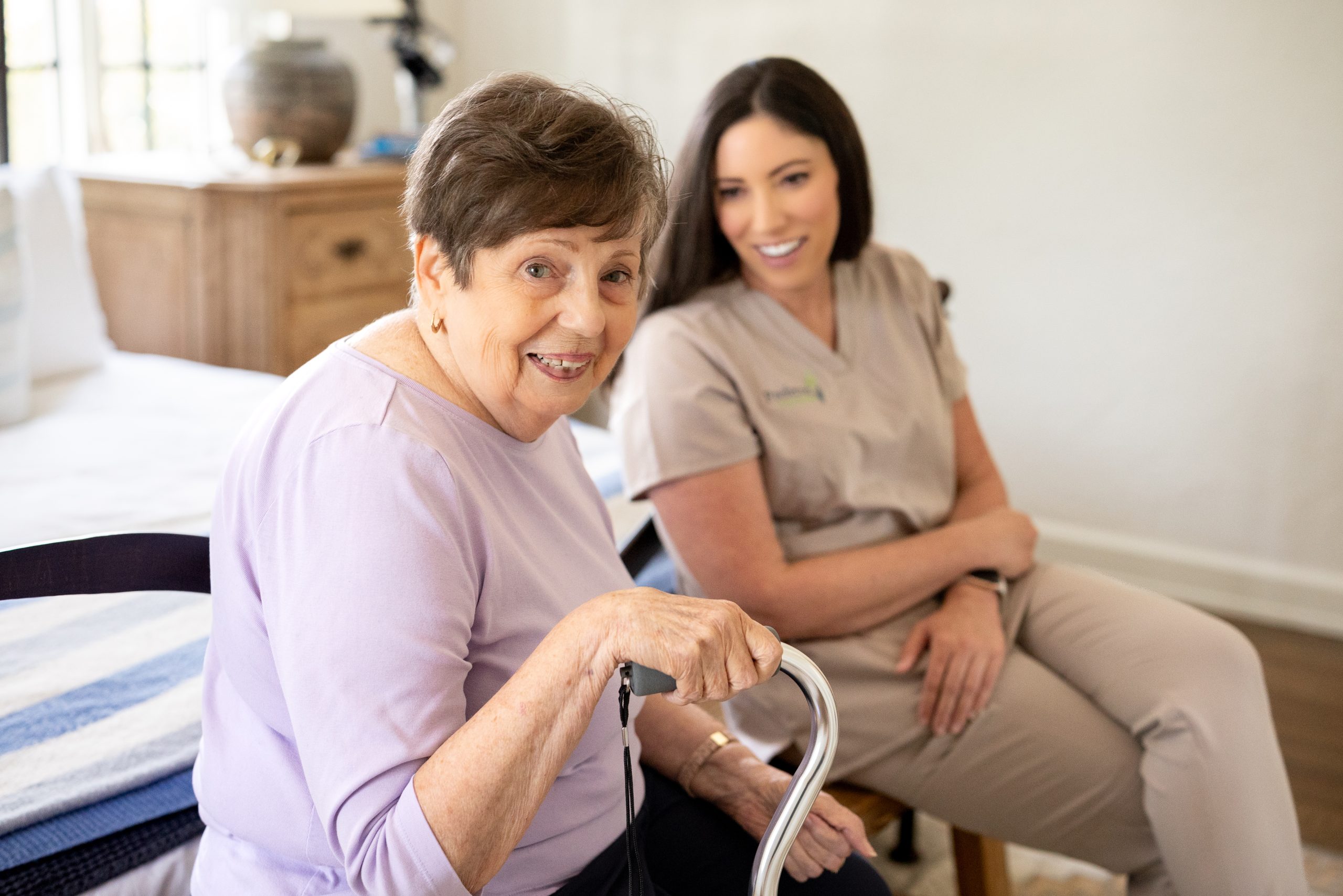 A woman with a walker sits beside an older woman, both engaged in conversation, highlighting live-in care support.