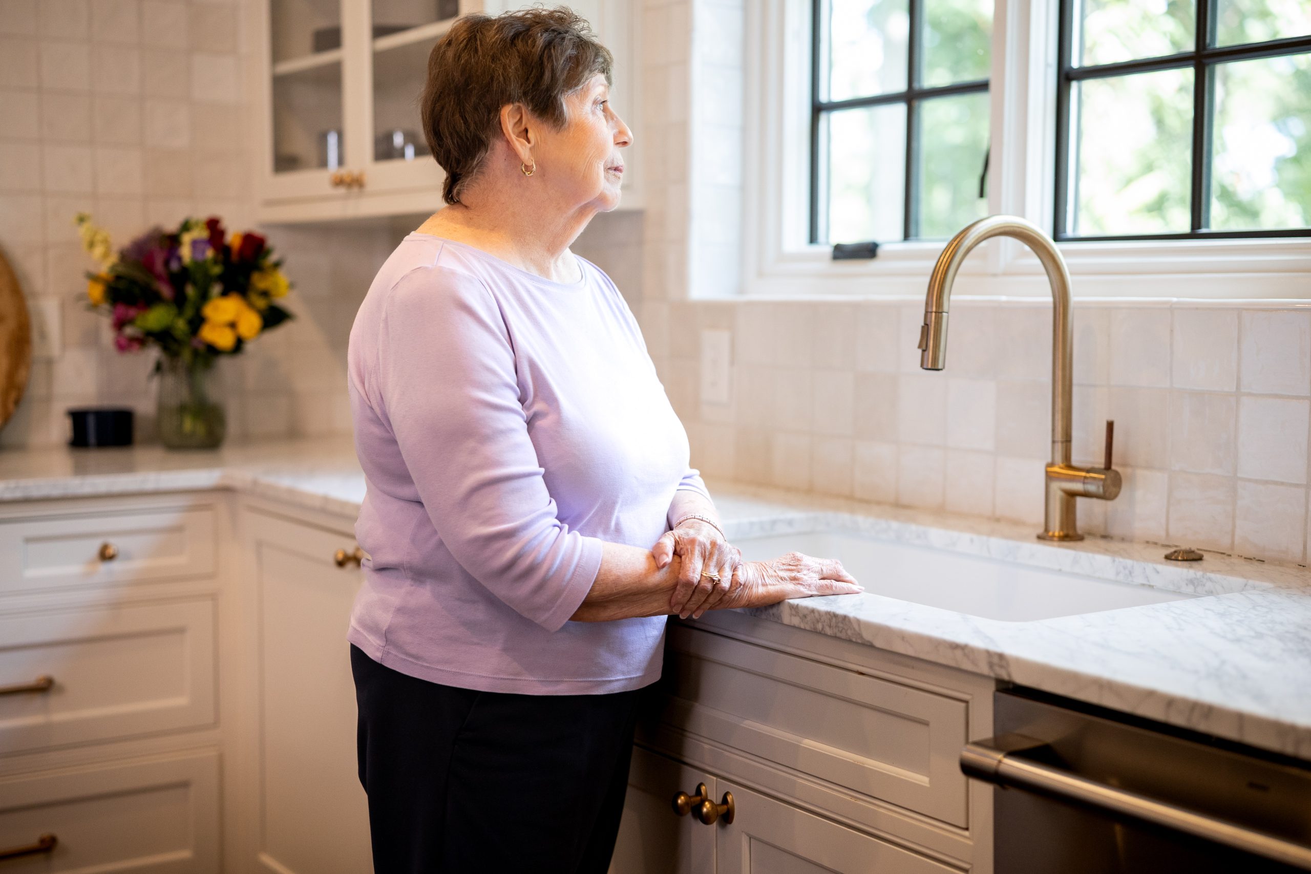 In a kitchen, a woman looks out the window, capturing a peaceful moment within a dementia care environment.