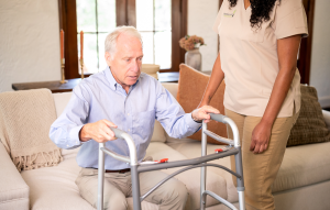 A woman assists an older man using a walker, providing support and guidance as they navigate together.