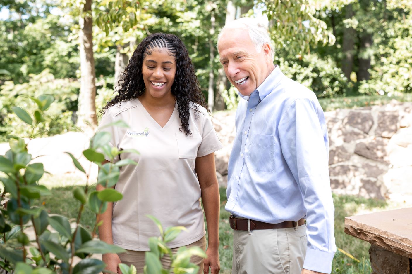 A man and woman pose in front of a vibrant bush, both looking cheerful and engaged.