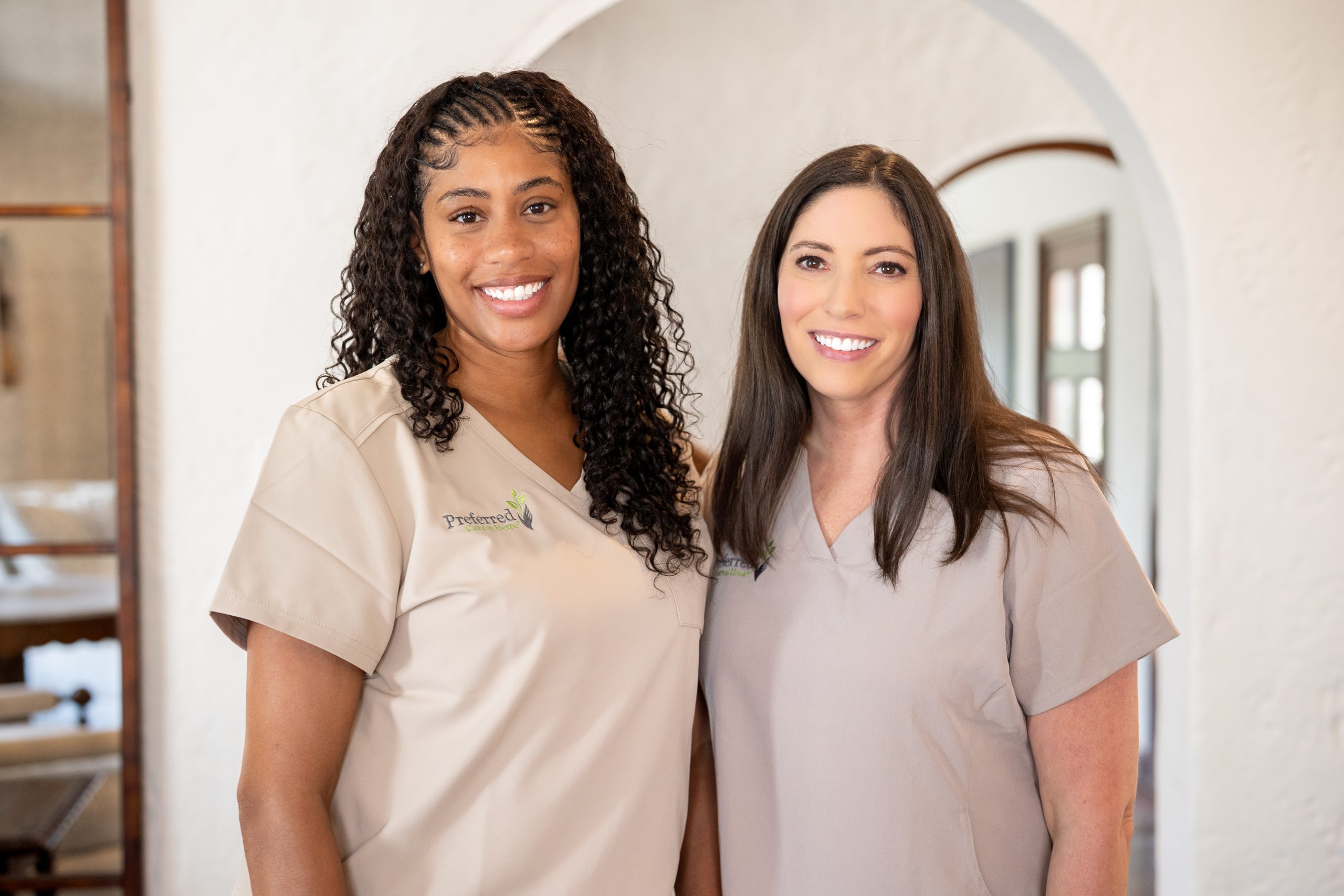 Two women wearing scrubs stand together, appearing friendly and professional in a medical environment.