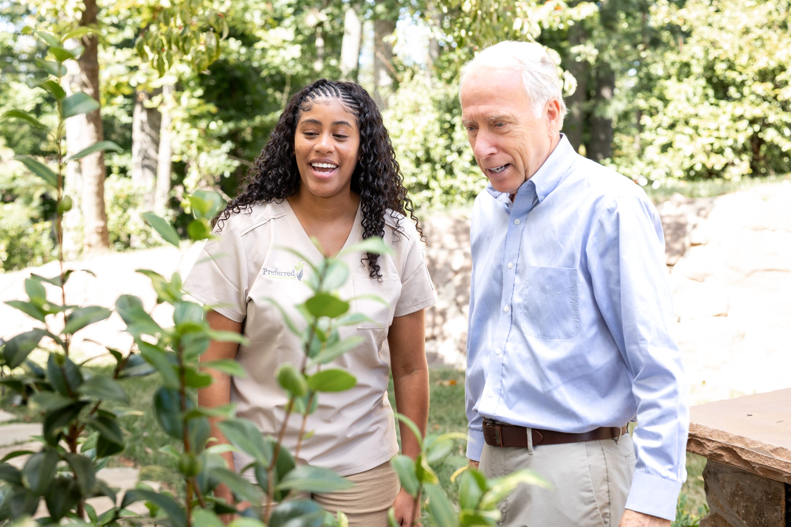 A man and woman pose in front of a vibrant bush, both looking cheerful and engaged.