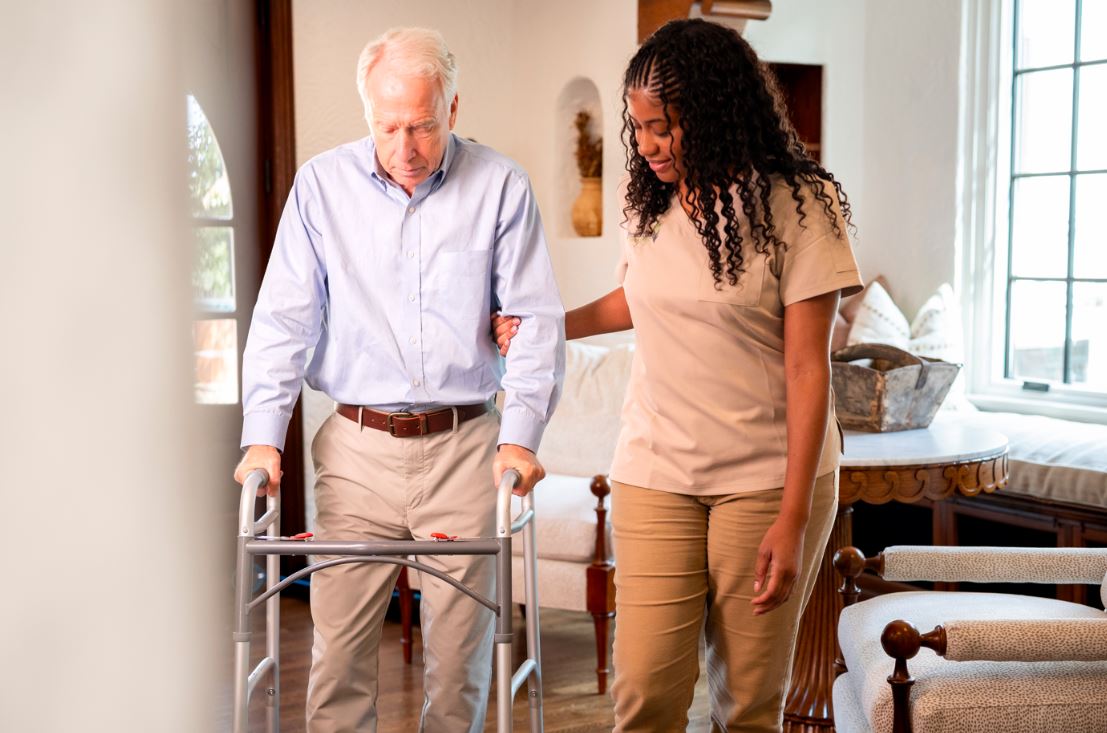 A woman assists an elderly man using a walker in a home setting, highlighting post-surgery care in San Antonio.