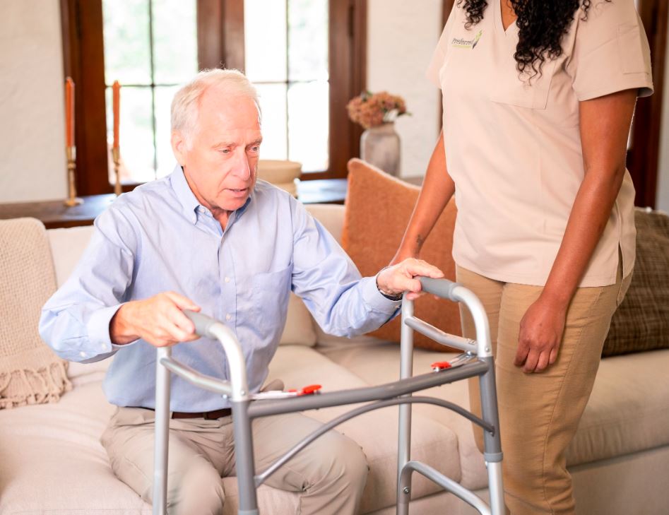 A woman provides support to an elderly man with a walker in a Transition Care facility, enhancing his mobility and independence.
