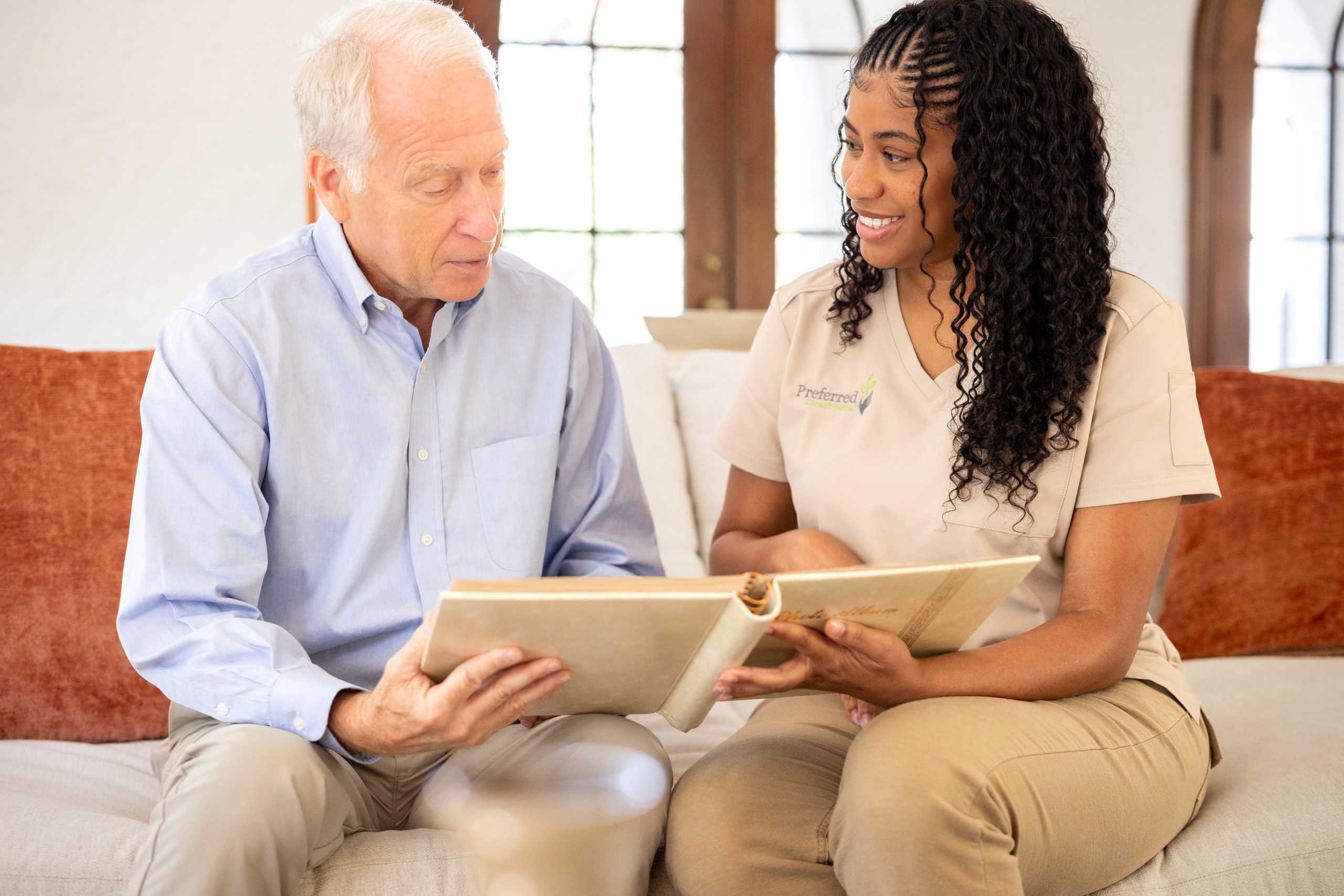 A woman and an older man sit on a couch, engaged in reading a book together, highlighting Alzheimer's care activities.
