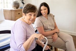 A woman with a walker sits beside an older woman, both engaged in conversation, highlighting companionship in live-in care.