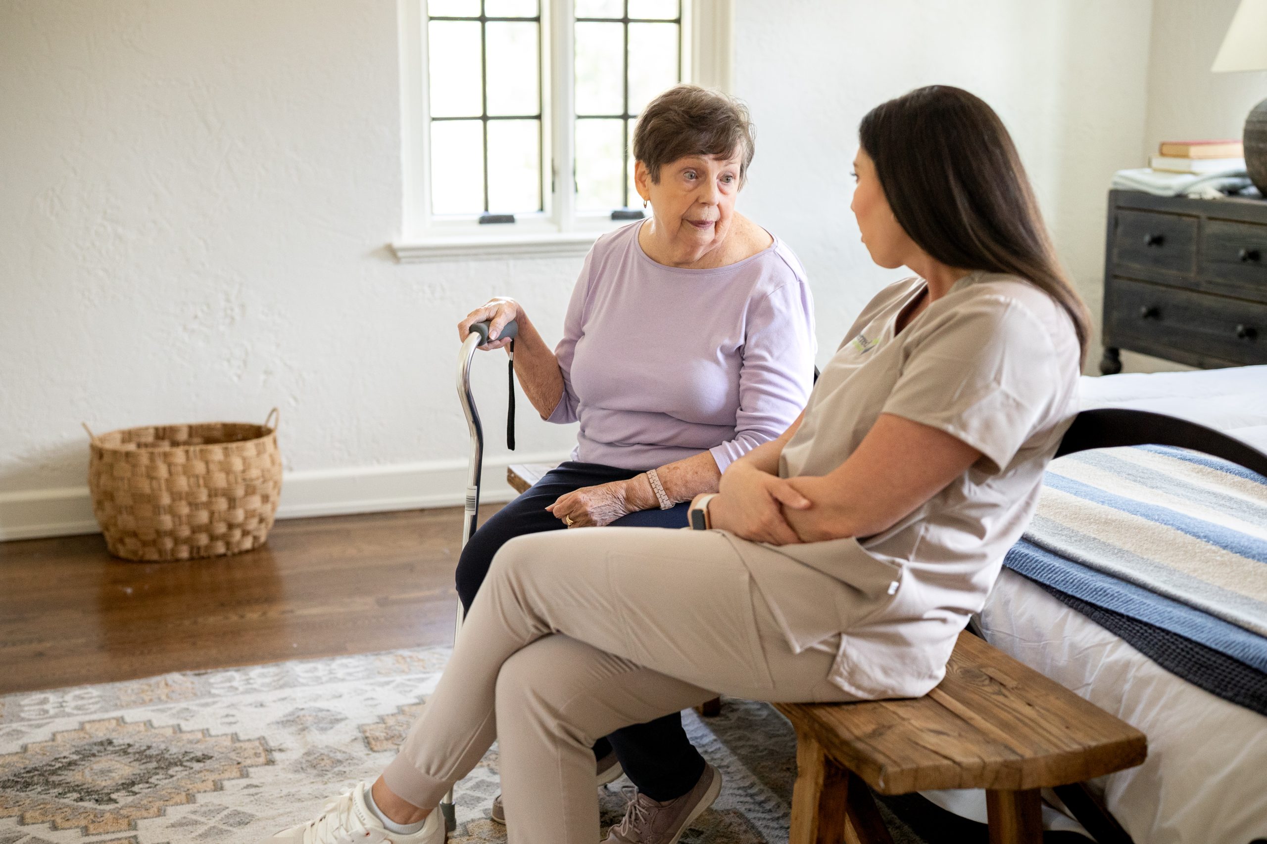 A woman talks to another woman in bed while seated on a bench, illustrating dependable care for seniors in Yonkers.